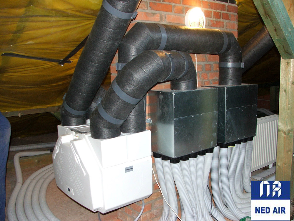 Kompletna instalacja wentylacyjna z rekuperacją w przestrzeni poddasza, widoczne izolowane rury wentylacyjne, skrzynki rozprężne i biała jednostka rekuperatora z licznymi elastycznymi przewodami.